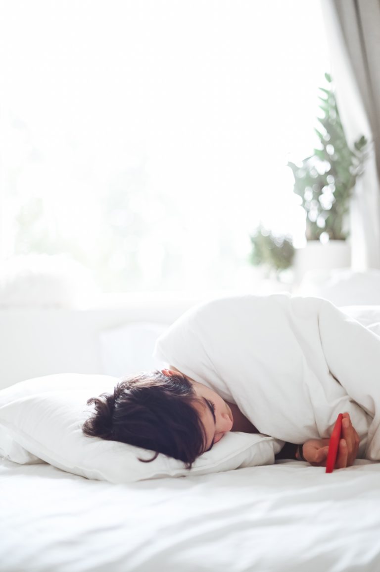Mujer descansando en la cama con el movil en la mano
