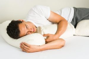hombre durmiendo de lado con almohadas blancas
