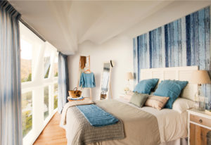 colchon con almohadas azules al frente de un ventanal