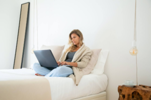 mujer sentada en la cama con una laptop en las piernas