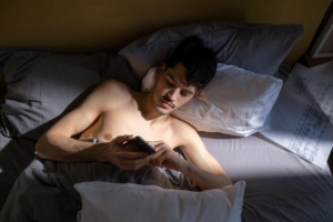 hombre sin camisa acostado en la cama con el movil en la mano