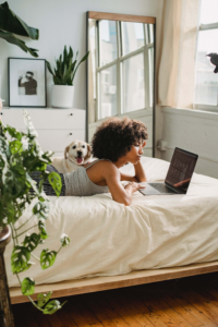 muchacha acostada en la cama con una laptop abierta y un perro 