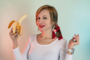 mujer sonriendo con una banana en la mano y una cinta roja en el cabello