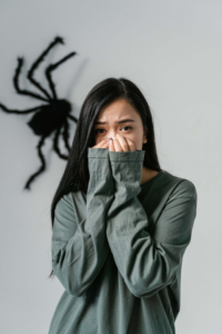 muchacha cabello negro con sweter verde las manos en la boca y una araña en la pared