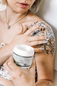 mujer con tatuaje en el hombro aplicando crema de cbd 