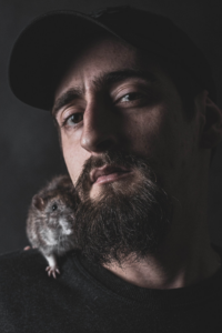 hombre con gorra, barba y una rata en el hombro