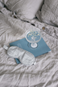 antifaz blanco, copa con agua tabla azul sobre la cama