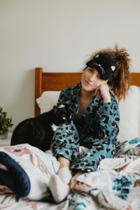 mujer con antifaz verde y un gato negro arriba de la cama