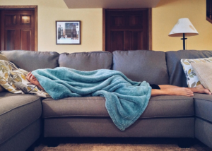 persona durmiendo en un sofa arropada con una manta azul