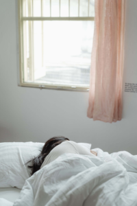 mujer durmiendo de lado con la ventana abierta y una cortina rosada de lado