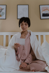 mujer leyendo un papel sentada en la cama con sabana blanca