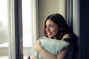 mujer sonriendo con una almohada abrazada frente a la ventana