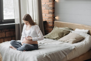 mujer sentada en la cama con las piernas cruzadas sobándose la barriga de embarazo 