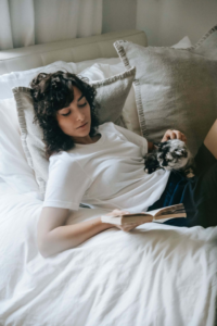 joven con un gato en las piernas leyendo un libro sobre la cama