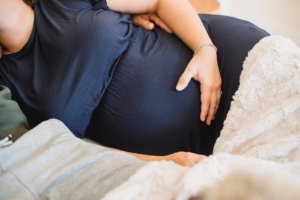 mujer embarazada con bluson azul durmeindo de lado con la mano sobre la barriga 
