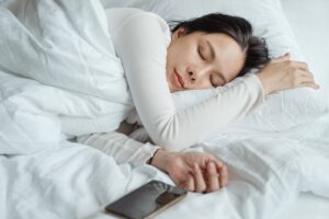 mujer dormida con el movil cerca de la mano sobre la cama