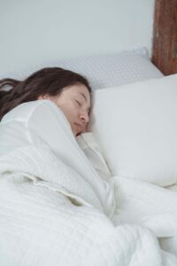 mujer durmiendo de lado sobre sabanas y almohadas blancas